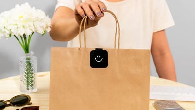 Adesivo personalizado para fechar sacola aplicado em embalagem de papel kraft, ideal para lacrar pedidos e reforçar a identidade da marca.