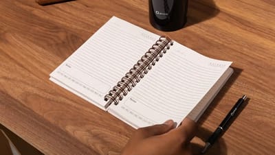 Agenda personalizada aberta sobre mesa de madeira com páginas pautadas para organização de tarefas e anotações.