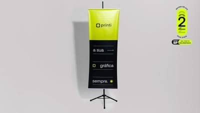 Banner de lona personalizado da Printi montado em suporte tripé preto, destacando o selo de entrega rápida em 2 dias úteis para São Paulo.