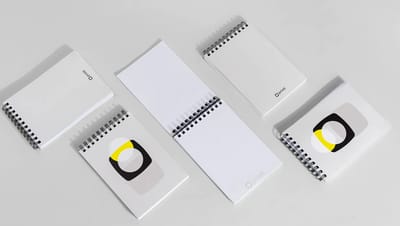 Diversas unidades de bloco de notas com capa wire-o espalhadas em ângulo, mostrando opções de capa personalizada e folhas internas brancas com o logotipo Printi.