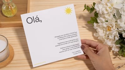 Mão segurando cartão de agradecimento da Printi com frase de gratidão, ao lado de uma caixa de papelão aberta com papel de seda, simulando uma experiência premium de unboxing para e-commerce.