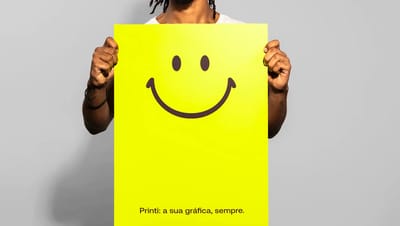 Homem segurando cartaz personalizado grande em amarelo neon com ícone de sorriso e a frase "Printi: a sua gráfica, sempre", demonstrando impacto visual.