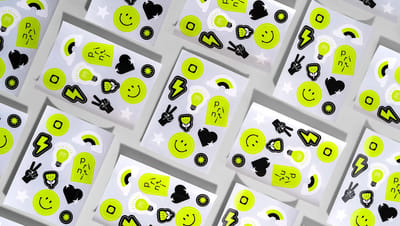 Cartela de adesivos personalizados com diversos formatos (raio, coração, sorriso) em verde neon e preto sobre fundo cinza.