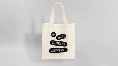 Ecobag de algodão cru personalizada com a frase "A sua gráfica, sempre" em tipografia preta, exibindo detalhe da alça e textura do material sustentável.