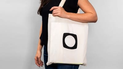 Mulher utilizando ecobag de algodão cru personalizada com logotipo preto da Printi, destacando o uso casual e sustentável do produto.