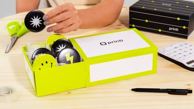 Mão abrindo embalagem gaveta personalizada da Printi em mesa de madeira, demonstrando a experiência de unboxing e a textura do material.