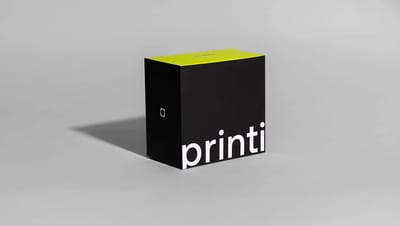 Embalagem personalizada da marca Printi nas cores preto e verde-limão, com logotipo branco, posicionada centralizada em um fundo neutro.