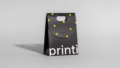 Embalagem sacola personalizada da Printi com design minimalista em preto, alça de mão recortada e fechamento em aba circular com estampa de bolinhas.