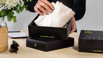 Mulher acomodando peça de vestuário em embalagem tampa e fundo personalizada da Printi, destacando o uso para e-commerce e unboxing.