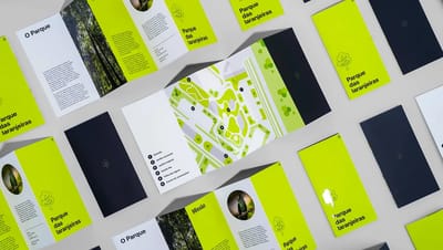 Mockup com várias unidades de folder 4 dobras em diferentes posições. Em destaque no centro, o folder aberto revela um mapa ilustrado com legenda dos pontos turísticos, demonstrando a paginação e o layout do material impresso.