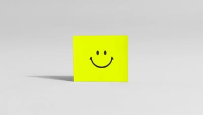 Ímã de geladeira quadrado na cor amarelo neon com estampa de emoji de carinha sorridente preta, centralizado em um fundo branco minimalista com sombra projetada lateralmente.