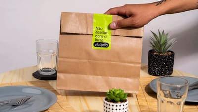 Lacre de segurança personalizado da Printi aplicado em embalagem de delivery de hambúrguer, com design preto e verde neon destacando a frase "Bom apetite" para garantir a integridade do pedido.