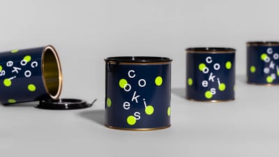 Quatro unidades de lata de metal personalizadas para cookies dispostas em diferentes ângulos, mostrando uma lata deitada com interior dourado e as outras em pé sobre fundo neutro.