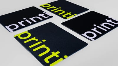 Detalhe de mouse pad personalizado retangular com a frase "A sua gráfica, sempre" em preto e amarelo sobre fundo cinza.
