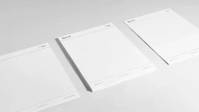 Três blocos de papel timbrado personalizado da Printi dispostos em perspectiva sobre fundo branco. Cada bloco exibe o logotipo no topo e o slogan institucional, destacando a produção em escala de papelaria corporativa profissional.