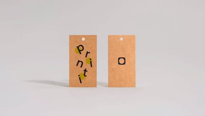Detalhe frontal e verso de tags personalizadas em papel kraft com logotipo da Printi, exibindo qualidade de furação e textura do material.