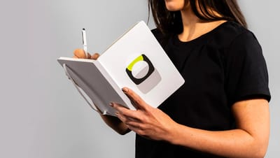 Mulher utilizando caderneta grande personalizada branca com logotipo centralizado para anotações.