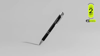 Caneta Metal Classic preta personalizada com o logo da Printi, posicionada na diagonal sobre fundo cinza claro. No canto superior direito, selo promocional verde com a informação de entrega em até 2 dias úteis na Grande São Paulo com frete relâmpago.