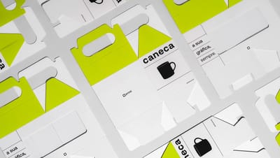 Embalagens para caneca em papel cartão branco com detalhes em verde neon, exibidas abertas sobre fundo neutro. As caixas apresentam recorte para alça, ilustração de caneca e o texto “caneca”, além da assinatura da Printi