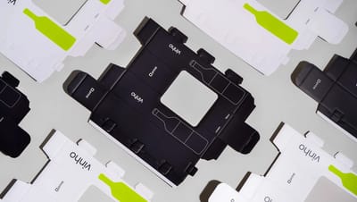 Embalagens personalizadas para vinho abertas e planificadas com design em preto e branco e detalhes verdes da Printi, mostrando estrutura de caixa para garrafa usada em presentes, eventos e vendas.