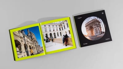 Fotolivro personalizado impresso com páginas abertas mostrando fotografias de viagem em layout editorial moderno e capa com foto do Arco do Triunfo em Paris.