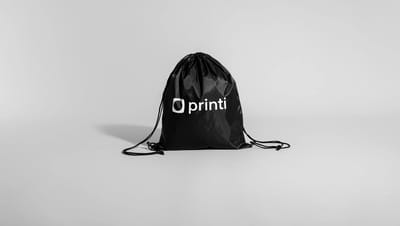 Mochila saco preta personalizada com logo branco da Printi, exibida em fundo branco e neutro.