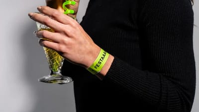 Pulseira de identificação personalizada verde sendo usada no pulso em evento, enquanto a pessoa segura um copo de bebida.