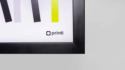 Detalhe de canto de quadro personalizado com moldura preta e logotipo Printi em fundo branco.