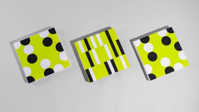 Três telas decorativas todas em formato quadrado com estampas de bolinhas e listras em preto, branco e verde-limão, posicionadas lado a lado sobre fundo cinza.