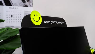 Testeira personalizada para monitor com comunicação visual promocional aplicada em ambiente de escritório.